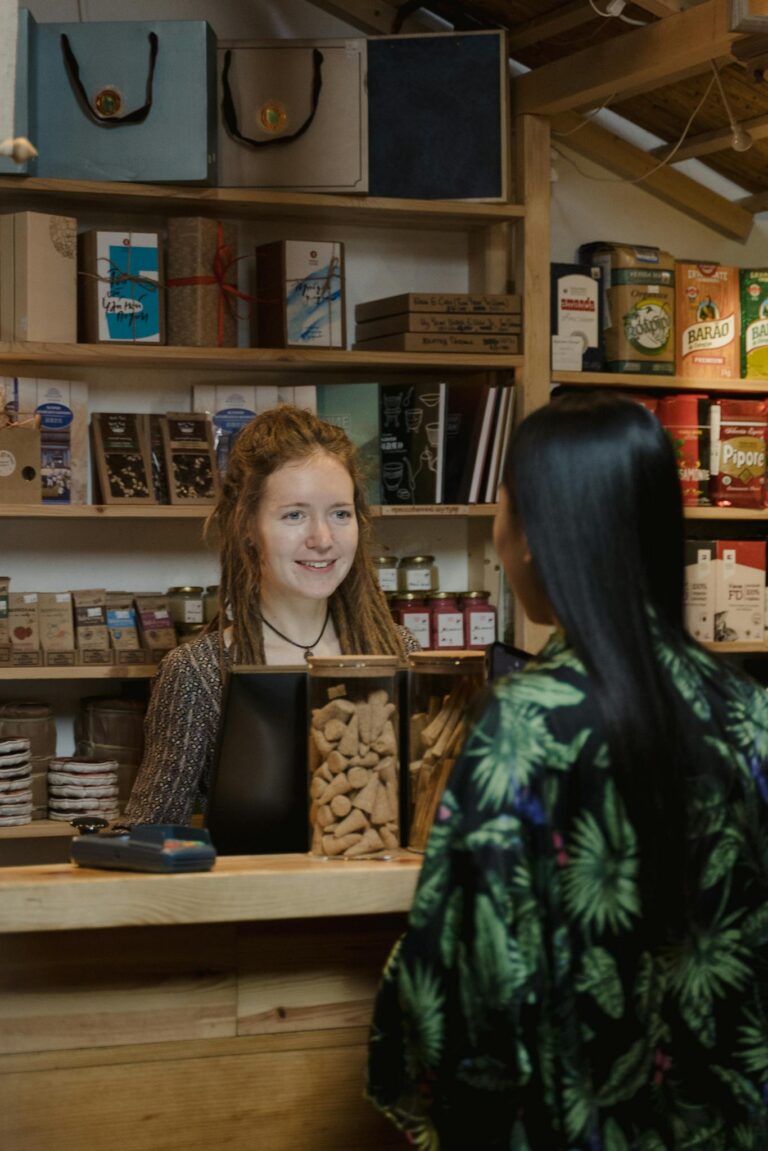 A customer exchanges smiles with a shopkeeper in a warm, inviting store environment.